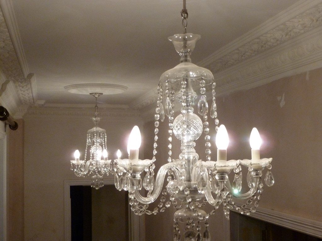 Two crystal chandeliers lit along a corniced ceiling