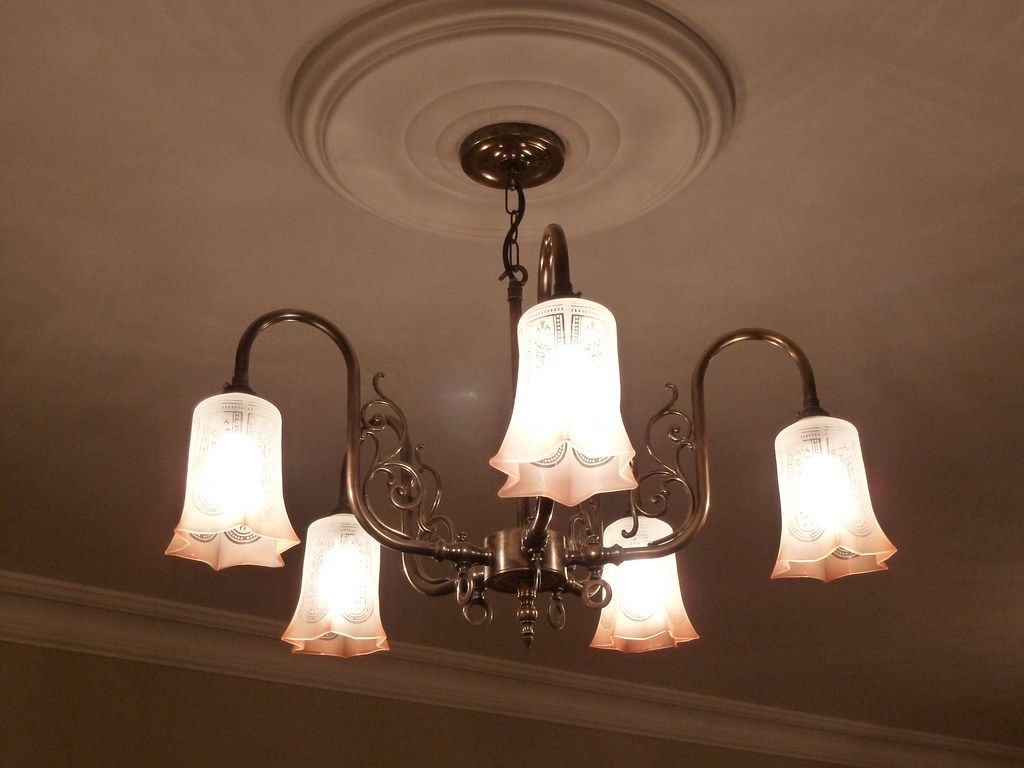 Five-arm brass light fitting with frosted tulip shades beneath a plaster ceiling rose