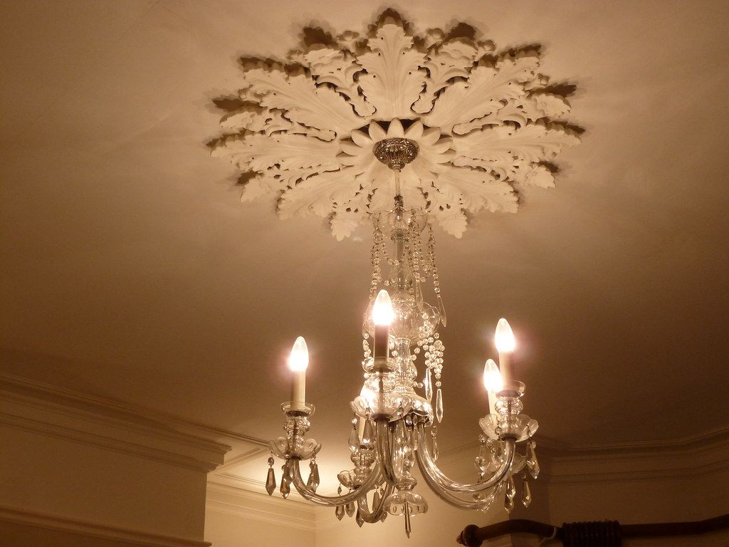 Candle chandelier lit beneath a large plaster ceiling rose in a warm room