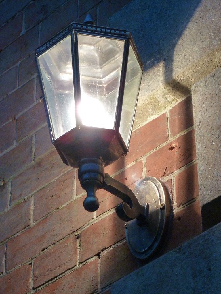 Black outdoor wall lantern lit against a brick wall