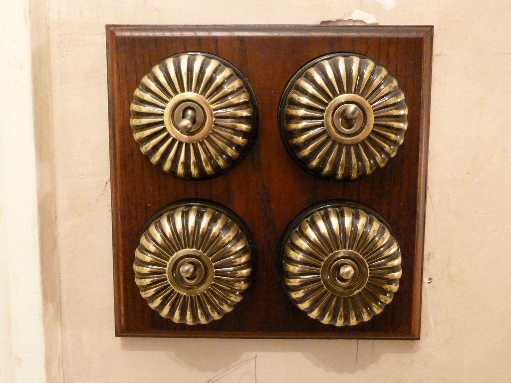 Four brass dolly switches on a dark wooden pattress