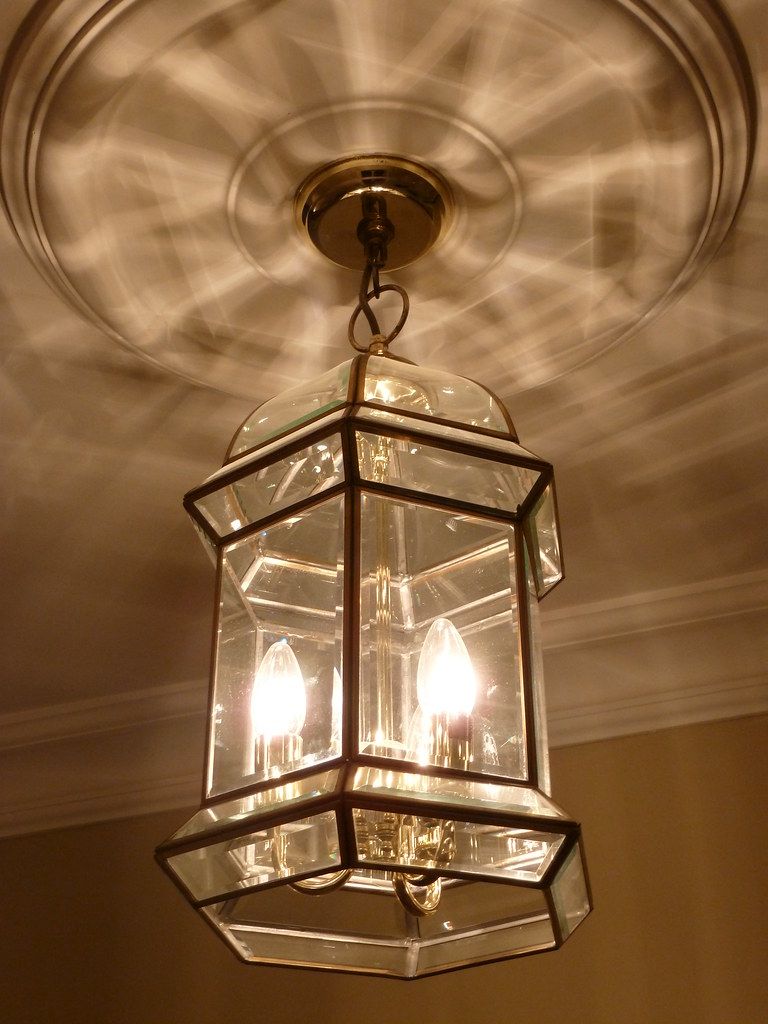 Glass and brass hall lantern lit beneath a ceiling rose